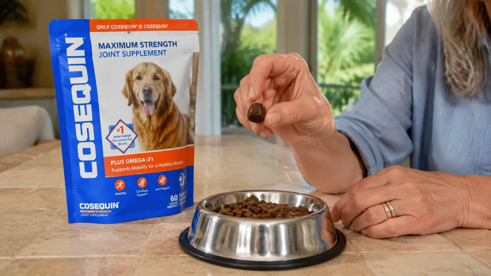 Hand holding a single Cosequin soft chew over a small stainless steel dog bowl with kibble